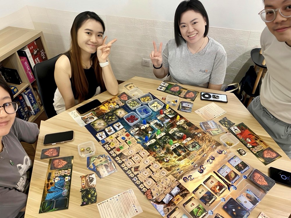 Four friends smiling around a sprawling board game at a Hexabox table